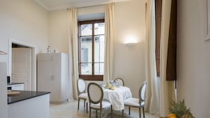 A dining area with a table set for four, a refrigerator, and a window with curtains.