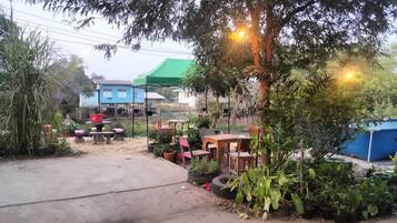 An outdoor patio area with tables and chairs, surrounded by potted plants and trees.