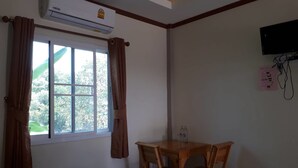 A room with a window, an air conditioning unit, a wooden table with chairs, and a flat-screen TV mounted on the wall. - Dome Resort (Sena)