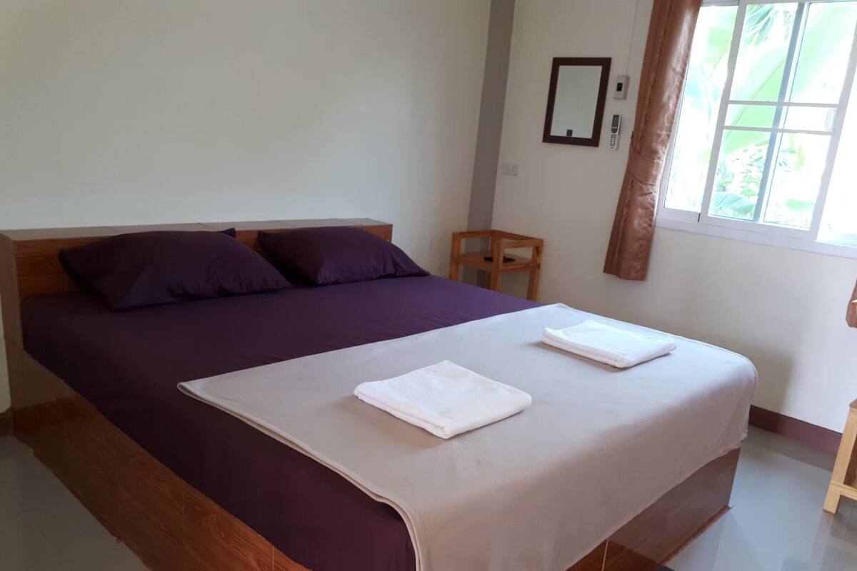 A single bed with a wooden headboard, a purple bedspread, and two white towels on the bed.