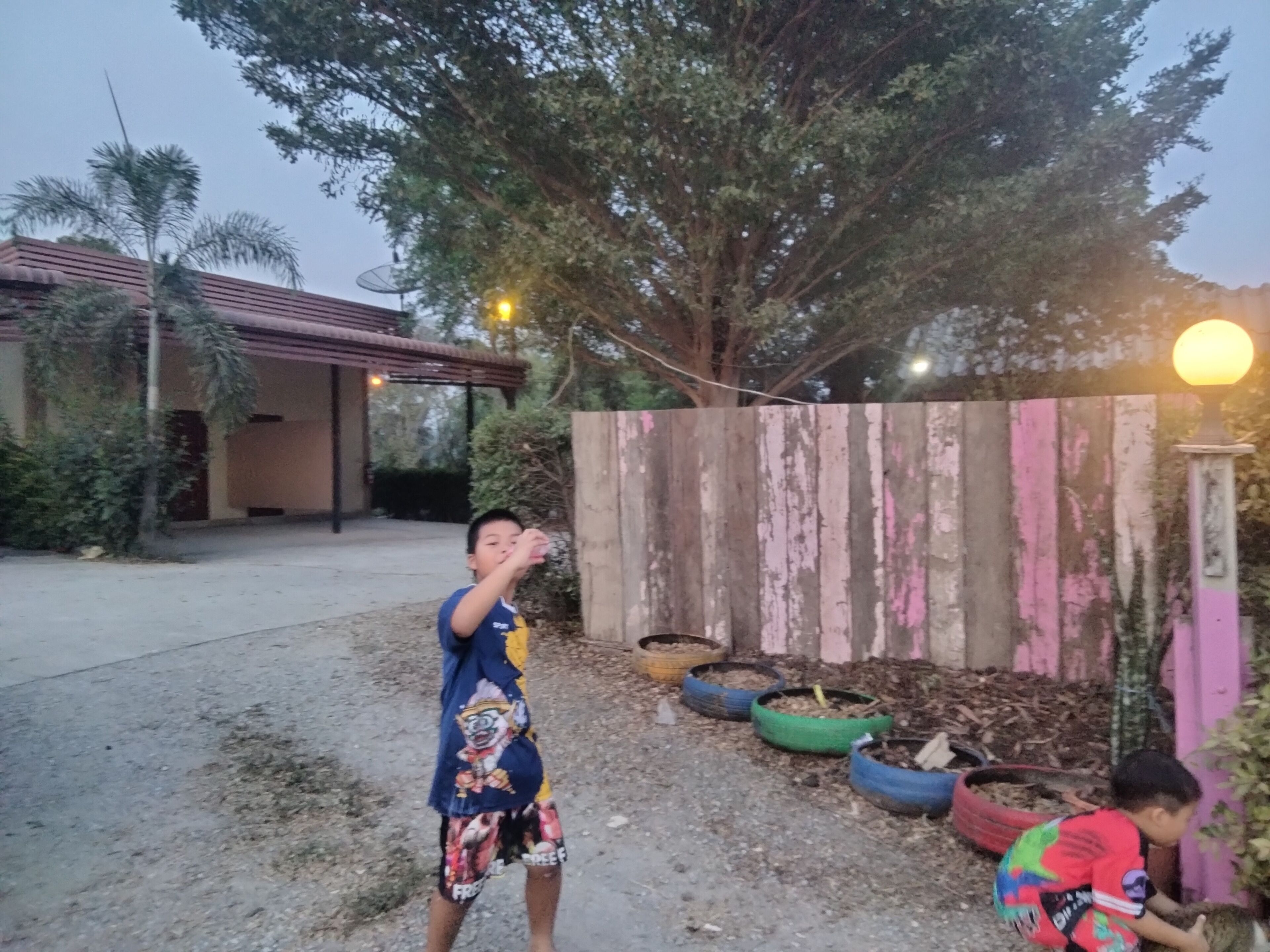 A child playing in a backyard with a wooden fence and tire planters.
