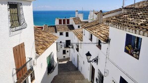 A narrow street with white buildings and terracotta roofs, leading to a view of the sea. - BOUGAINVILLEA HOUSE. COSTA VALENCIANA, COSTA BLANCA Pool, Garden, Beach, Villages. (Daimús)