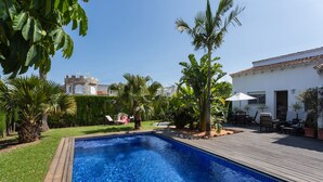 A swimming pool with a wooden deck, surrounded by greenery and a white building with a tiled roof. - BOUGAINVILLEA HOUSE. COSTA VALENCIANA, COSTA BLANCA Pool, Garden, Beach, Villages. (Daimús)