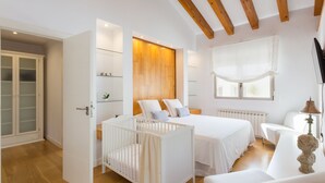 A bedroom with a crib, two beds, a wardrobe, and a window with curtains. - BOUGAINVILLEA HOUSE. COSTA VALENCIANA, COSTA BLANCA Pool, Garden, Beach, Villages. (Daimús)