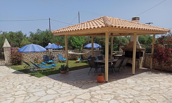 Um pátio com piso de pedra, pérgola, mobiliário para área externa e espaço para churrasco.
