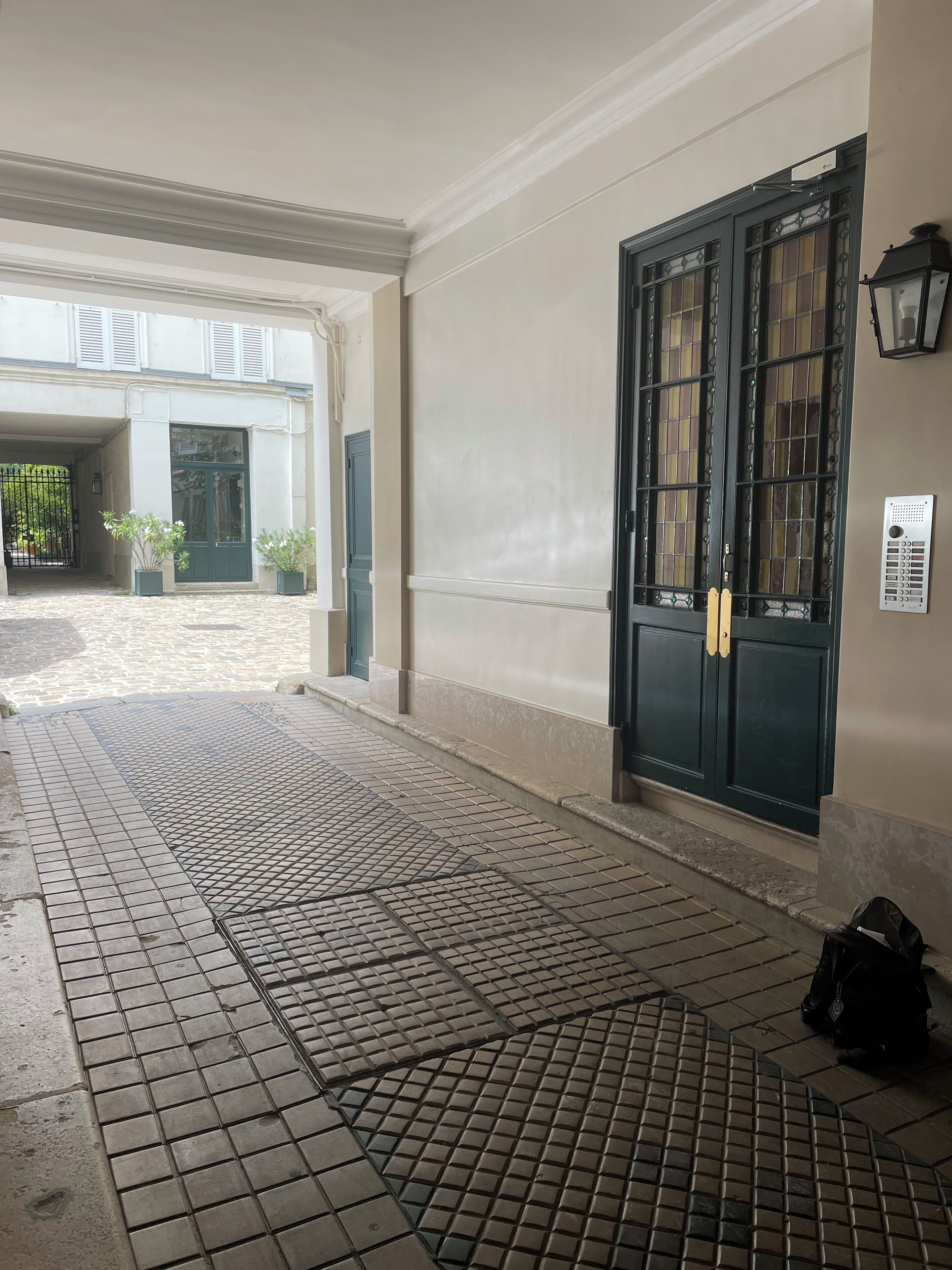 A clean, tiled entrance area with a large dark door, a small potted plant, and a wall-mounted light fixture.