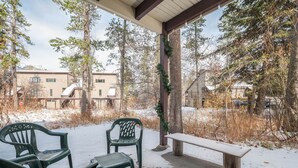 Katettu ulkoalue, jossa on kaksi vihreää muovituolia ja puinen penkki. Alue on lumen ja puiden ympäröimä.