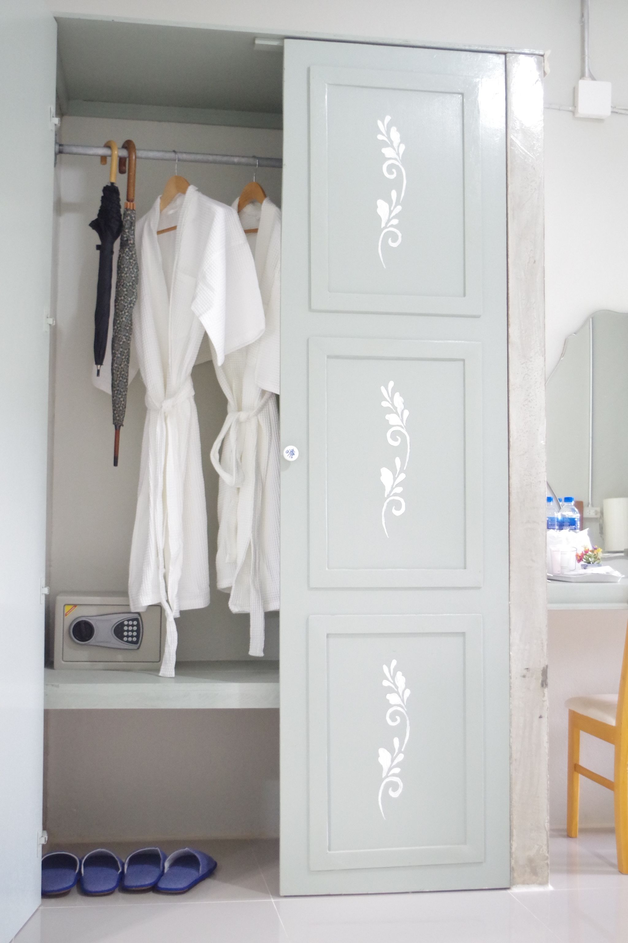 A wardrobe with two white robes hanging on wooden hangers, a pair of sandals on the floor, and a small shelf with a radio and a bottle.
