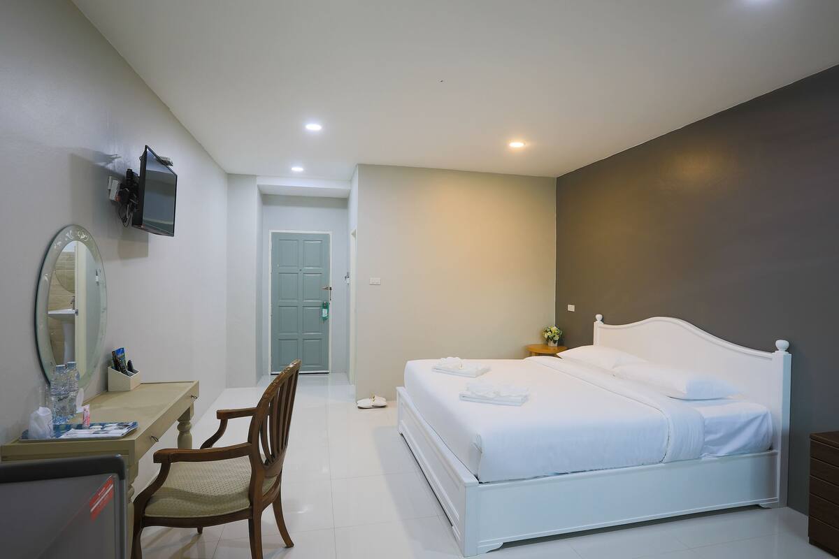 Habitación de hotel con cama, escritorio, silla, televisión montada en la pared y puerta que da a otra habitación.