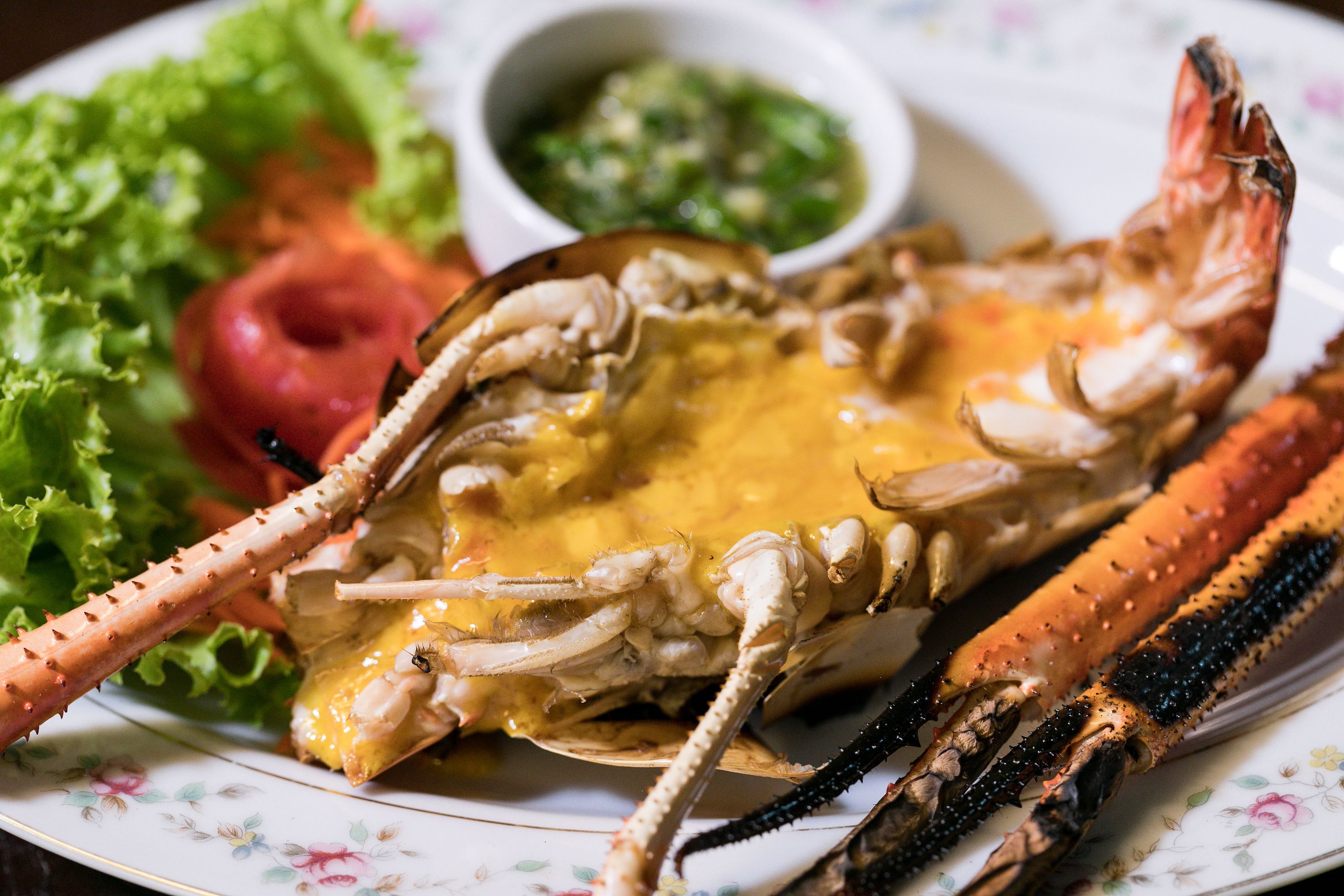 A plate with a cooked crab, a side salad, and a small bowl of sauce.