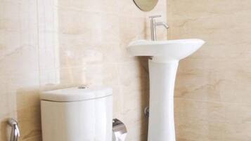 Une salle de bain équipée d’un WC, d’un lavabo, d’un miroir et d’une étagère en verre.