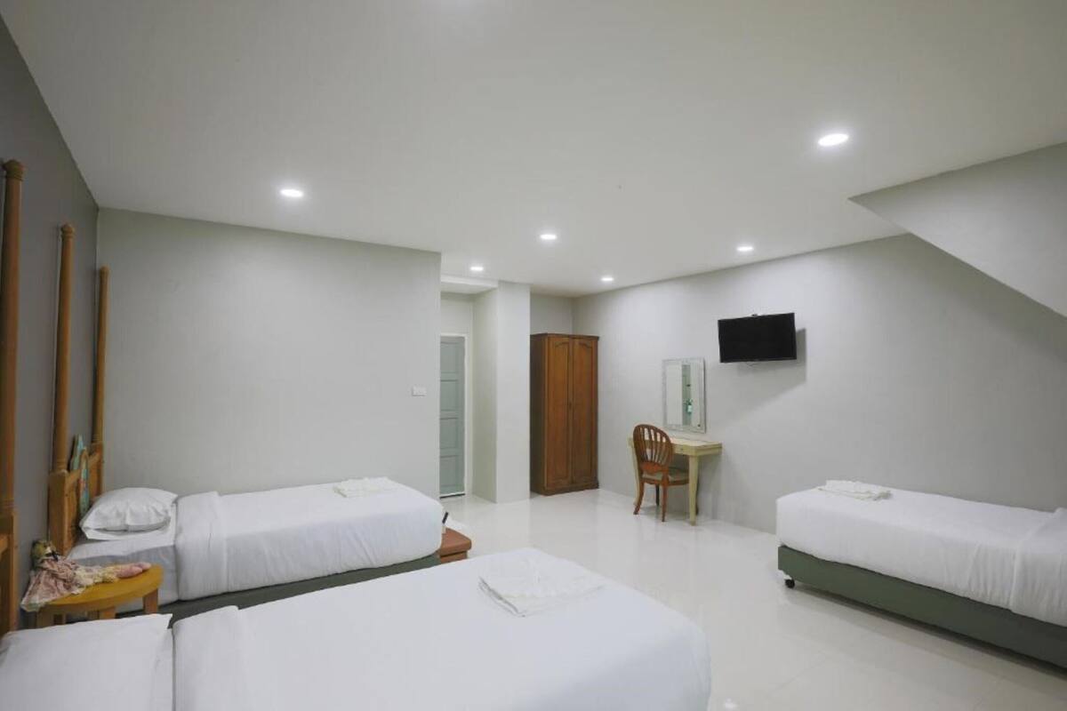 Habitación de hotel con tres camas individuales, un escritorio, una silla, un televisor montado en la pared y una puerta que da a otra habitación.
