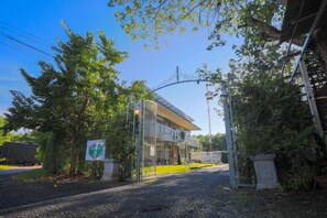 Un bâtiment doté d’une entrée fermée par un portail, entouré d’arbres et bordé d’une allée gravillonnée.