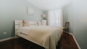 Ein Schlafzimmer mit einem großen Bett, einem Nachttisch, einem Sessel und einem Fenster mit Vorhängen.
