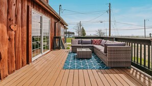Eine Holzterrasse mit einer Couch und Hocker, einem blauen geometrischen Teppich und Blick auf den Strand.