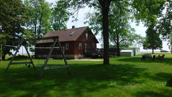 A wooden house with a porch, a swing set, and a covered seating area.