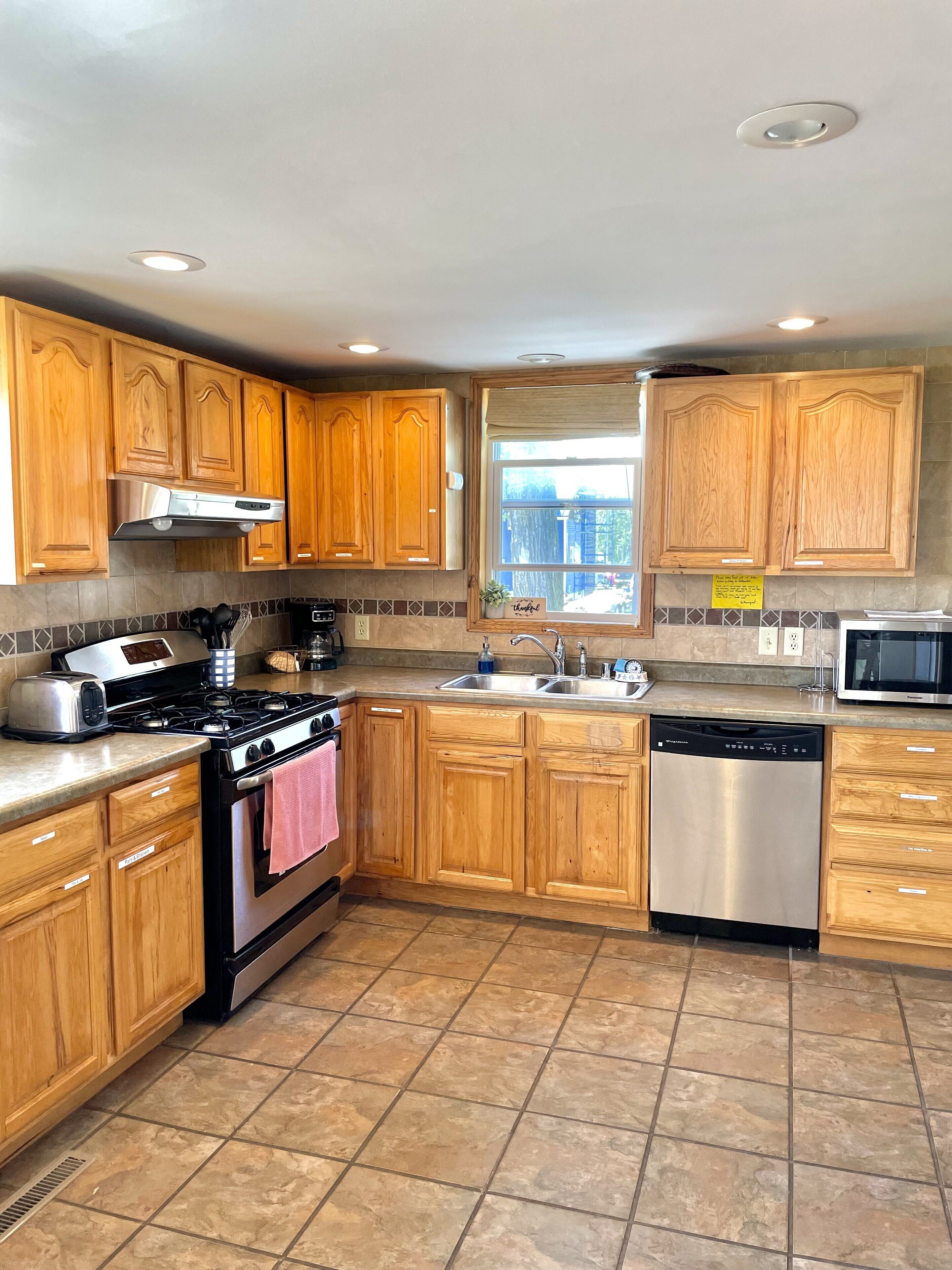 A kitchen with wooden cabinets, a stainless steel range, a dishwasher, and a window with a view.