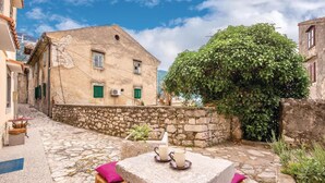 A stone-paved courtyard with a table and chairs, a building with green shutters, and a large ivy-covered tree. - Cozy apartment in Bakar with WiFi (Bakar)
