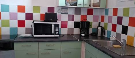 A kitchen with green cabinets, a microwave, a coffee maker, and a sink.