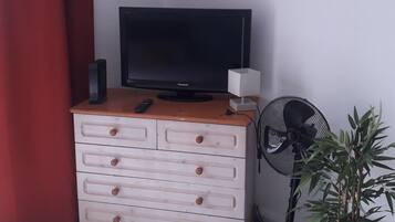 Una habitación con un aparador de madera, televisión, control remoto, ventilador y una planta en maceta.
