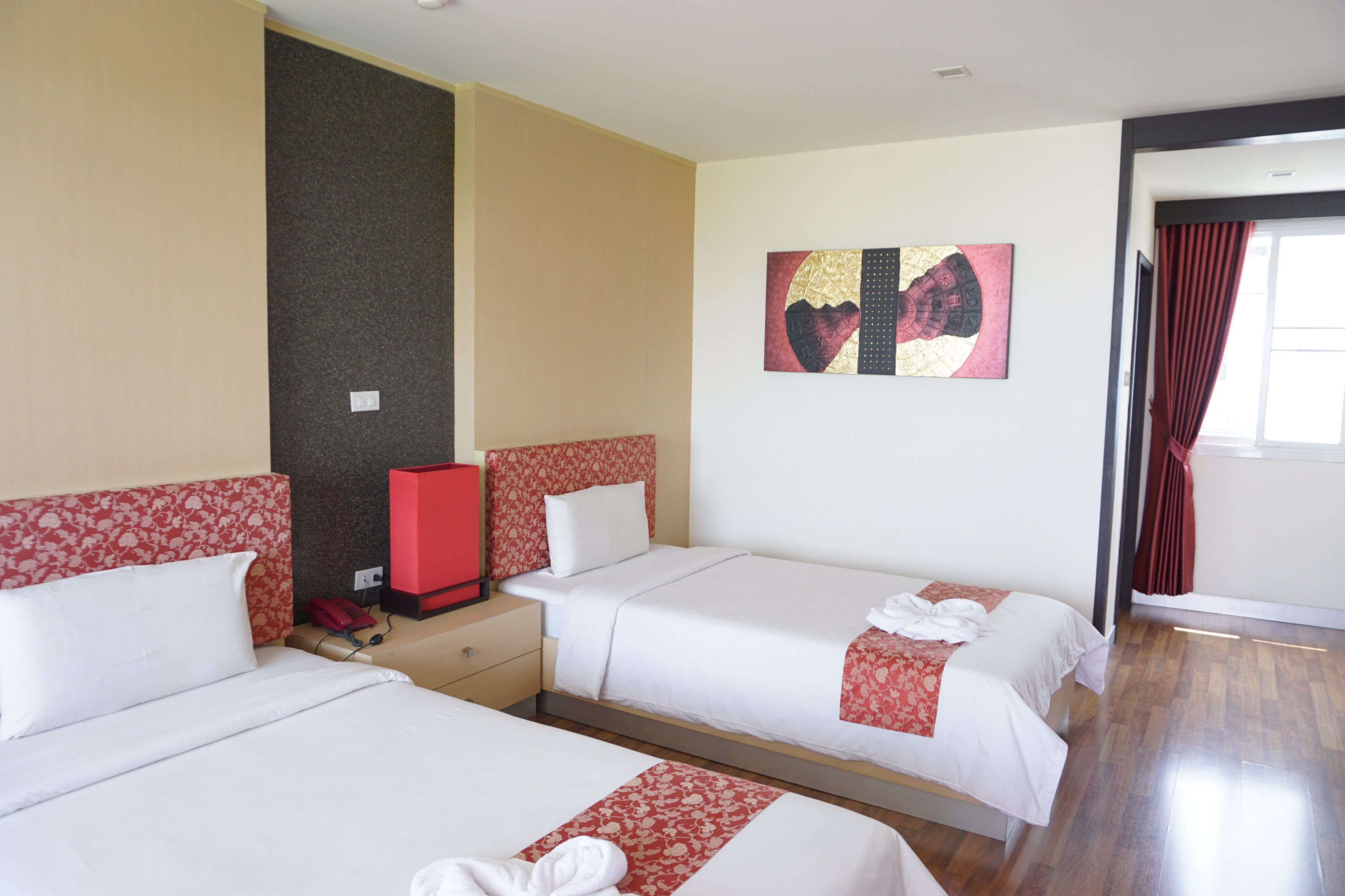 Quarto de hotel com duas camas, um minibar vermelho e um quadro na parede.