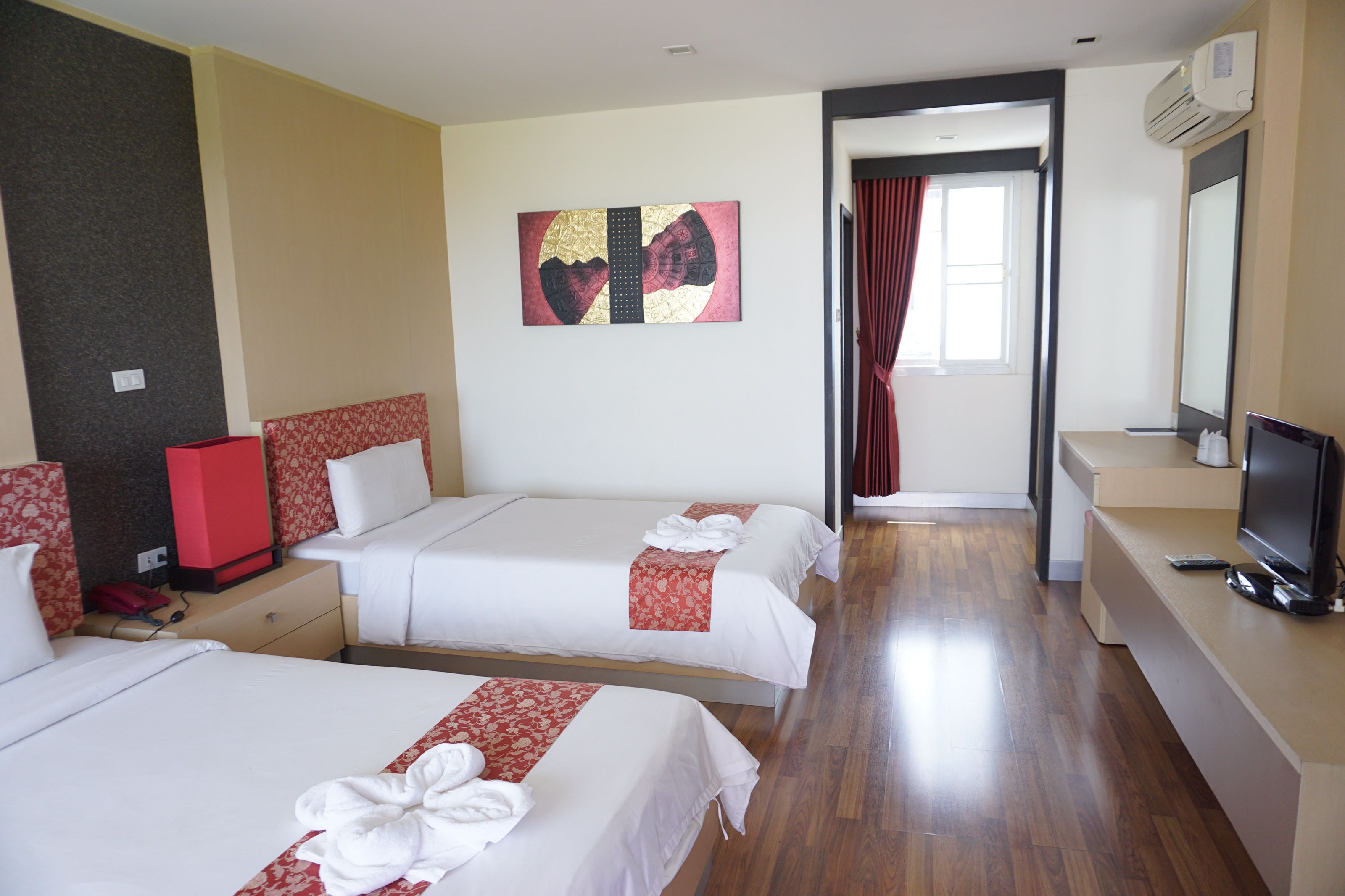 A hotel room with two beds, a TV, a desk, and a bathroom visible through an open door.