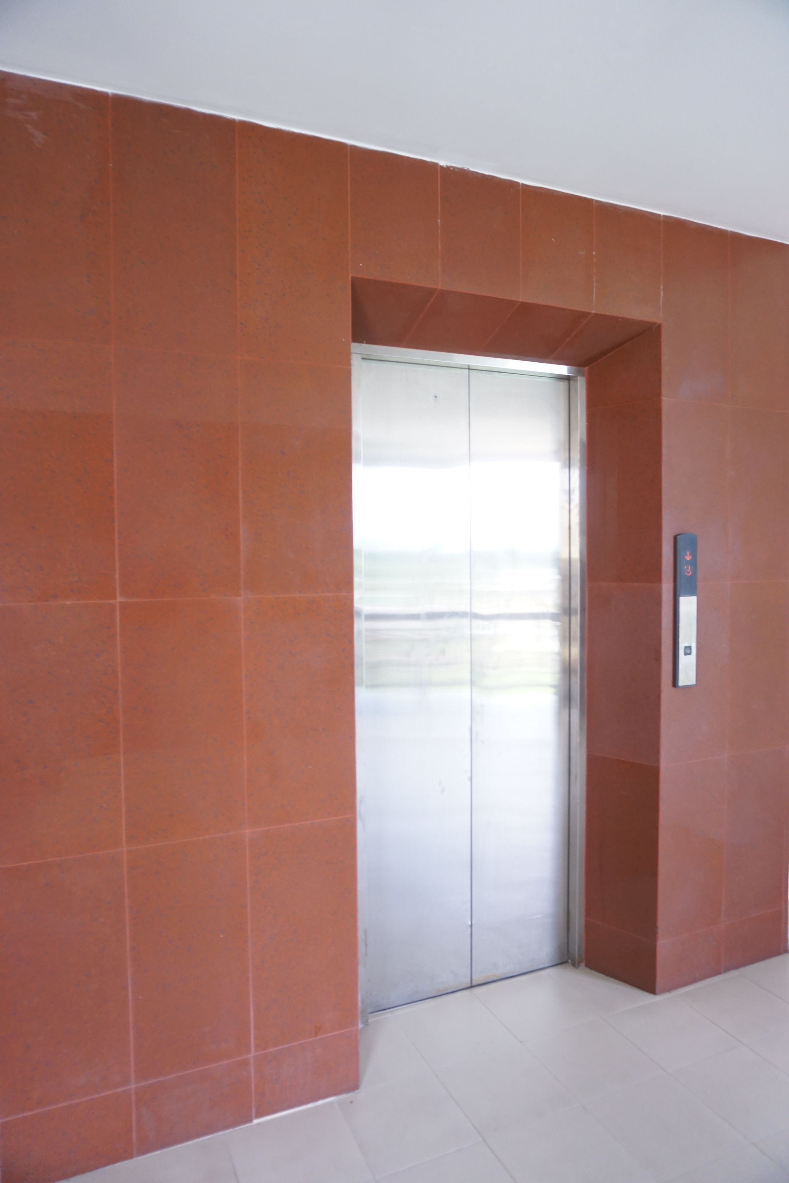 A modern elevator with a metallic finish, surrounded by orange-tiled walls and a white floor.