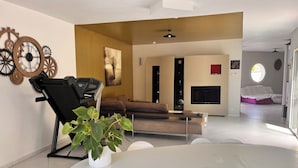Una sala de estar moderna con una caminadora, una planta grande, un sofá y un televisor.