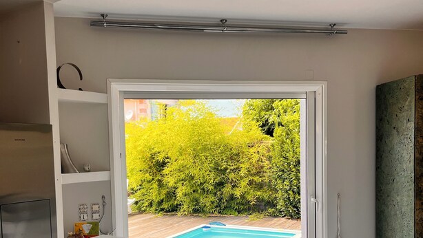 Cocina moderna con horno empotrado, encimera blanca y vistas a una piscina a través de un ventanal.