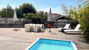 Una terraza de madera con piscina, sillas de descanso blancas y una mesa con sillas.