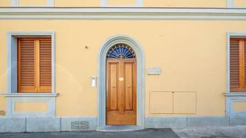 Un edificio con una porta in legno, una finestra con persiane e una piccola targa apposta al muro.
