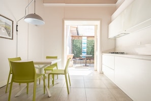 A modern kitchen with white cabinets, a dining area with green chairs, and a view of a garden through an open door.