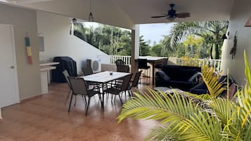 Un patio techado con mesa y sillas, ventilador de techo y una parrilla.