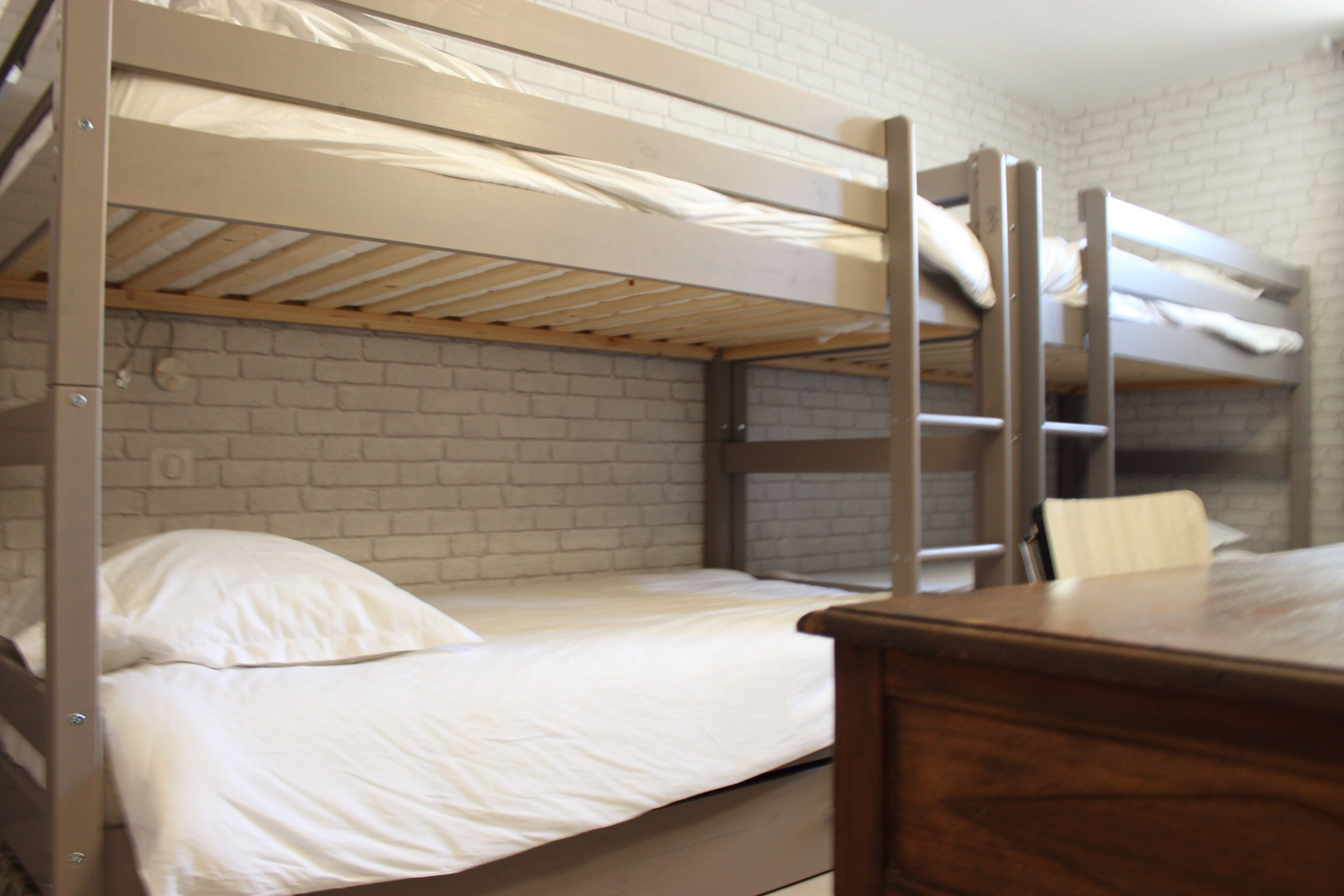 A bunk bed room with a brick wall and a wooden desk.