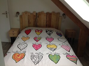 A bedroom with a wooden slat headboard, a bed with a heart-patterned bedspread, and two bedside tables. - Saint Malo, large house with garden 15 pers. 400m thermal baths and beach of the furrow (Saint-Malo)