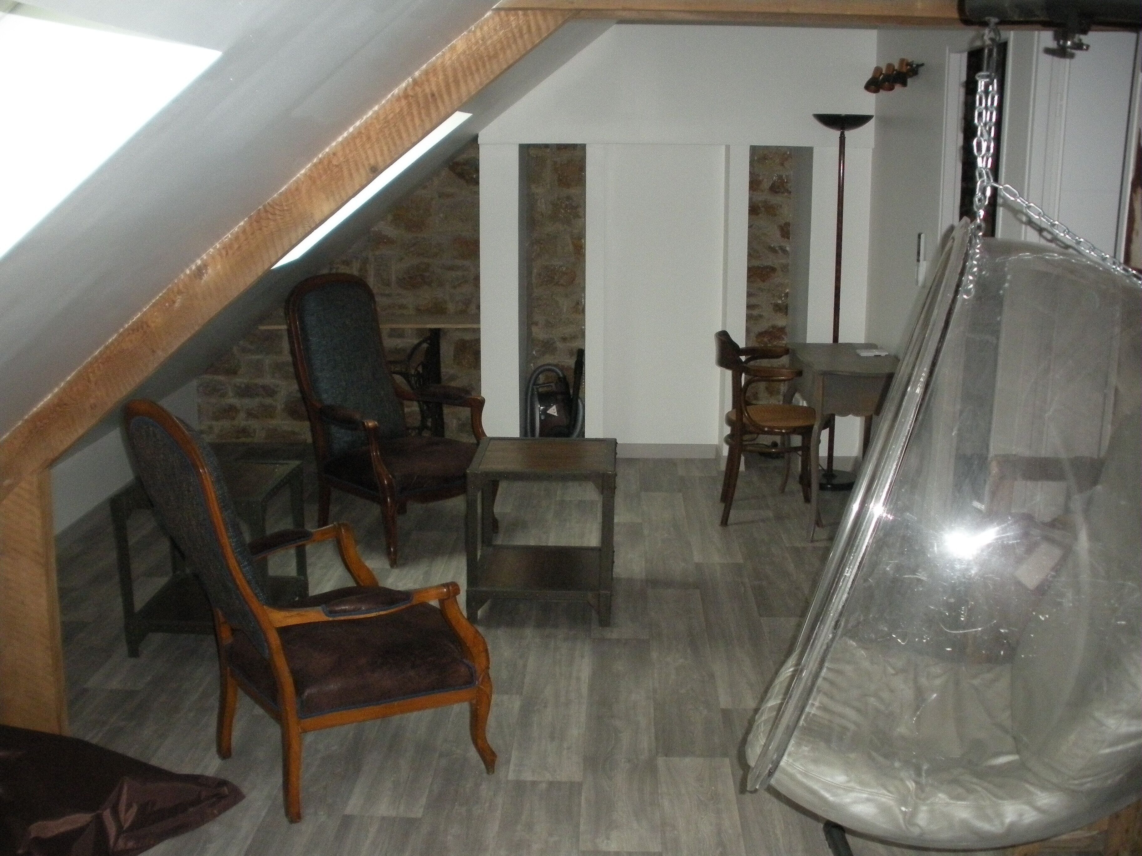A loft-style room with a stone wall, wooden ceiling beams, and a hanging chair.