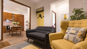 A living room with a sofa and armchair, a dining area with a table and chairs, and a kitchen with wooden cabinets.