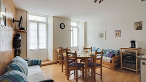 A cozy living room with a sofa, dining table, and chairs. There is a kitchen area with a microwave and a coffee machine. - Central Apartment with 1 Bedroom, Ski Locker, Near Lift (Cauterets)