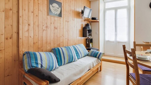 A wooden-paneled room with a sofa, a television, a coffee machine, and a dining area. - Central Apartment with 1 Bedroom, Ski Locker, Near Lift (Cauterets)