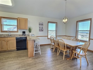 A modern kitchen with wooden cabinets, a dishwasher, and a dining area with a table and chairs.
