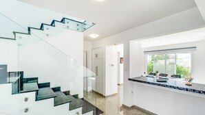 A modern interior with a glass staircase, a kitchen area with a tiled backsplash, and a view through a window. - Villa Aqua Marina by Ezoria Villas (Protaras)