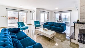 A spacious living room with a blue sofa set, a coffee table, and a fireplace. - Villa Aqua Marina by Ezoria Villas (Protaras)