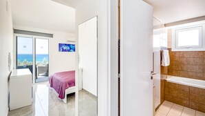 A modern hotel room with a bed, a view of the sea, a bathroom with a bathtub, and a door leading to another room. - Villa Aqua Marina by Ezoria Villas (Protaras)
