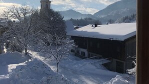 Schneebedeckte Landschaft mit einer Kirche und Gebäuden, einem klaren Himmel und Bergen im Hintergrund.