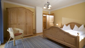 Ein Schlafzimmer mit einem hölzernen Bett, einem Korbstuhl, einem großen Kleiderschrank und einem Streifen Teppich.