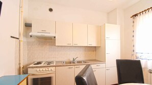A compact kitchen with white cabinets, a stove, a sink, and a refrigerator.