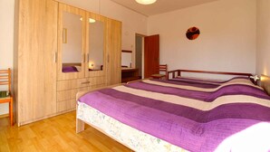 A bedroom with a large wardrobe, a bed with a striped bedspread, a chair, and a desk.