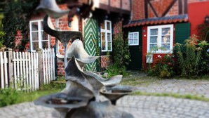A courtyard with a fountain, a white picket fence, and a red brick building with a green door and windows. - 2017 ecologically renovated, high quality furnished cottage with yard. (Lüneburg)