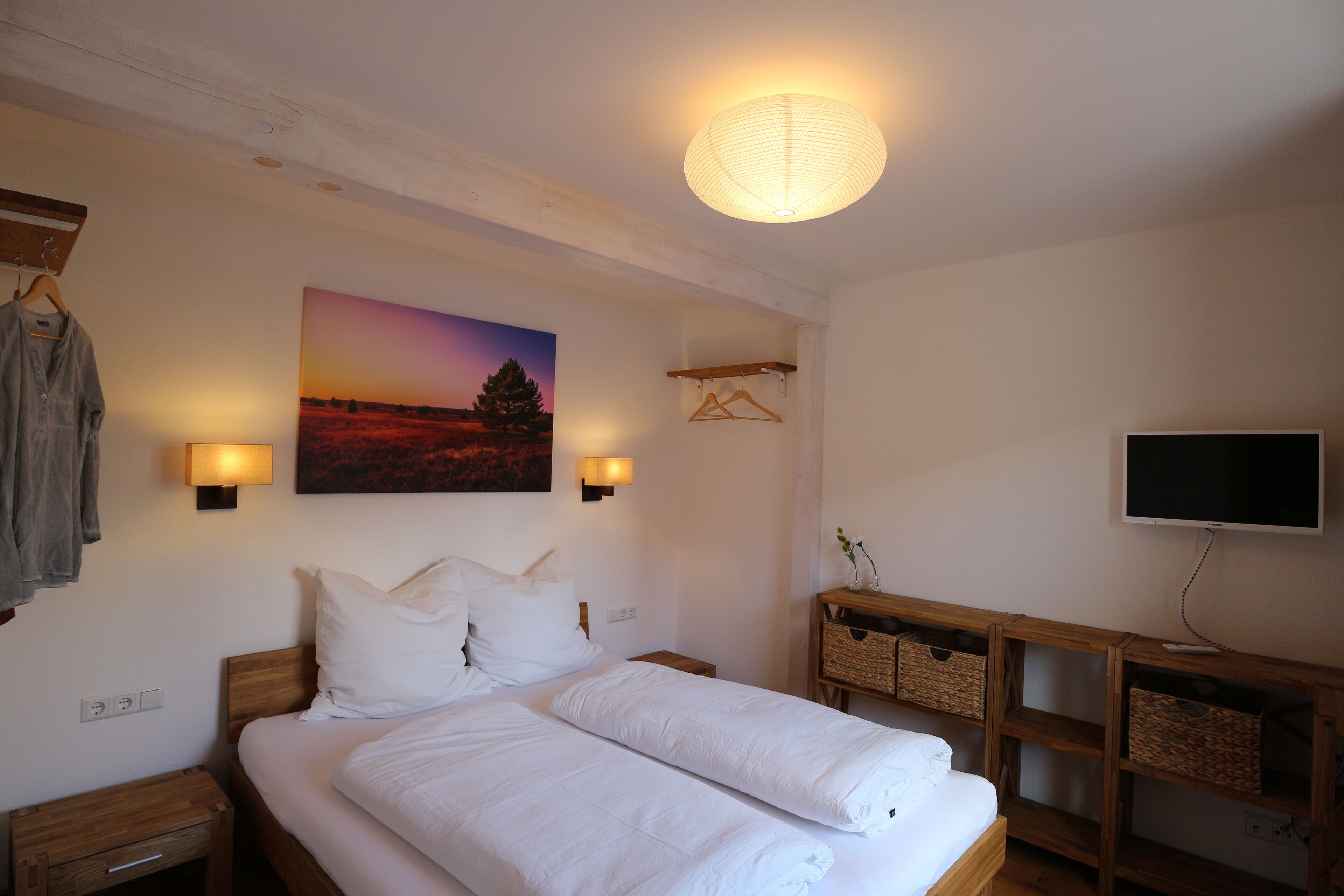 A bedroom with a bed, bedside tables, a wall-mounted TV, and a painting.
