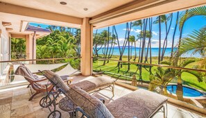 A balcony with a view of the ocean, a pool, and a lawn with palm trees. - FIVE BEDROOM BEACHFRONT SOUTH MAUI HOME - MODERN! (Kihei)